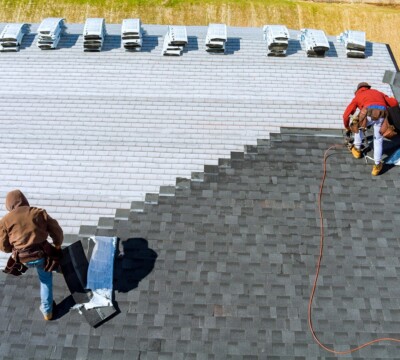 Aerial view in worker hands installing bitumen roof shingles with air hammer and nail